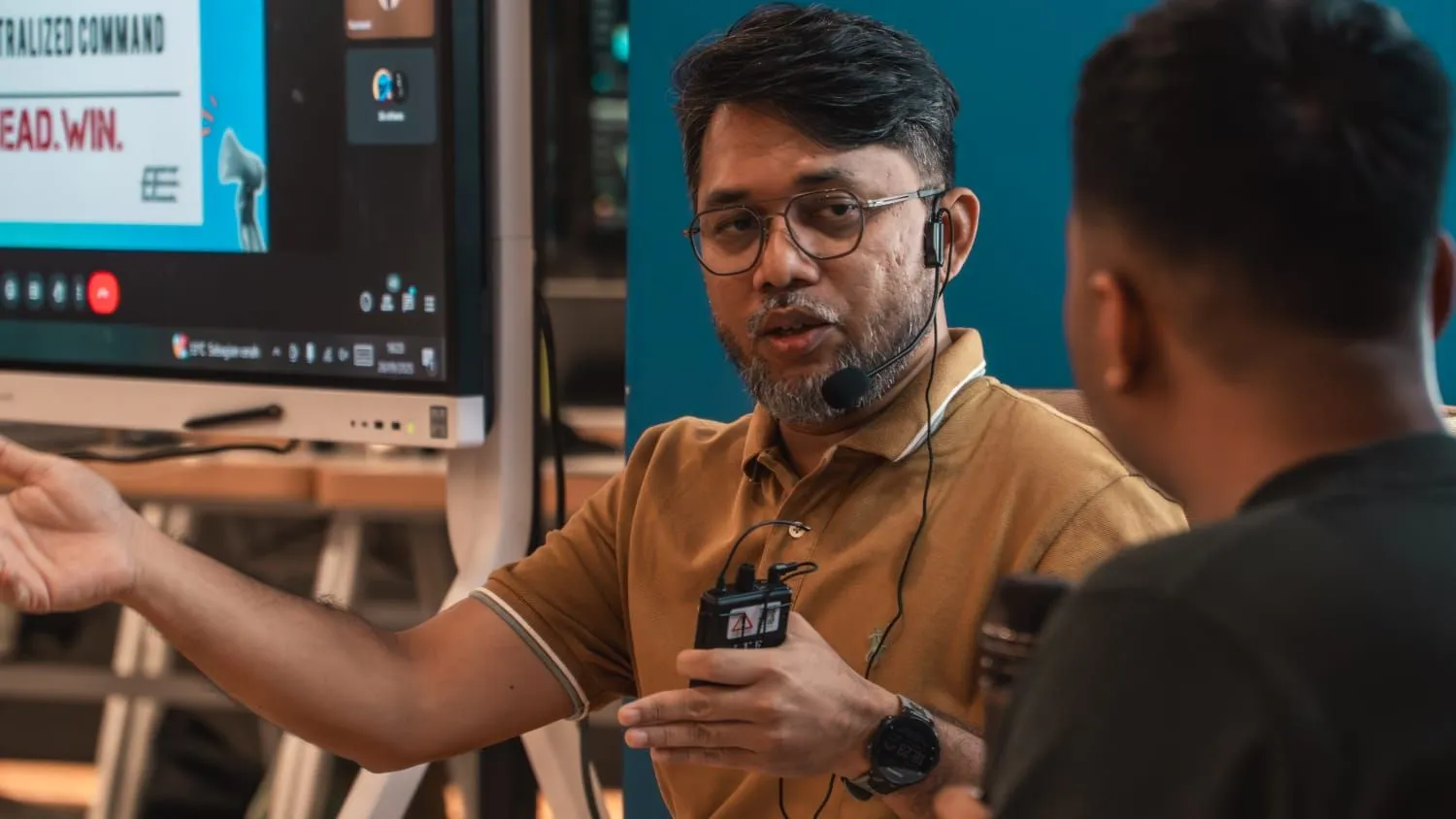 Hazmi wearing a headset microphone and explaining a point at Kreditplus Tech Lounge.